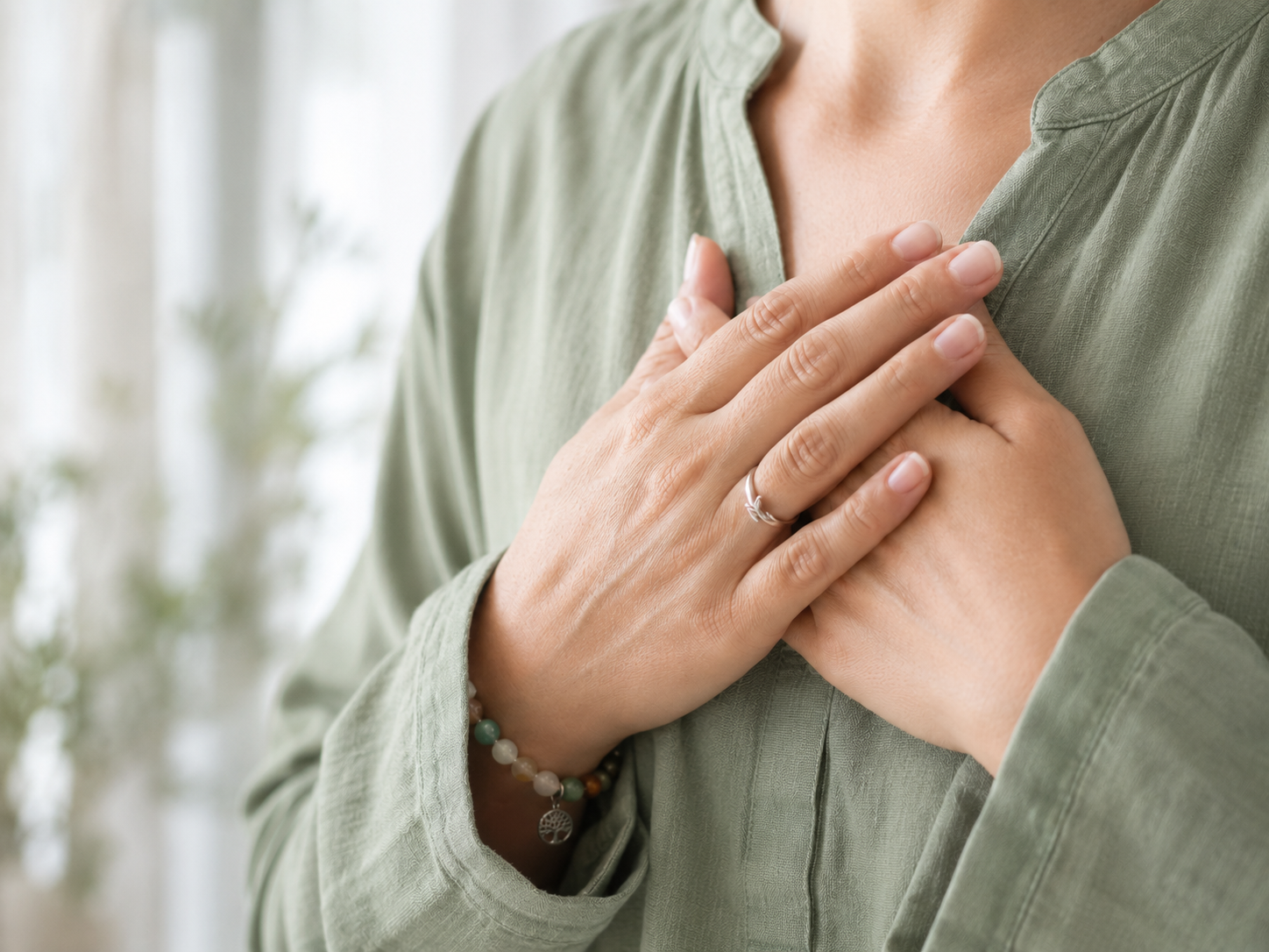 Mãos sobre o peito em camisa verde sálvia, gesto de acolhimento e presença